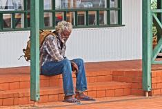 First Nations man sitting on brick steps. His face is turned towards the ground. 