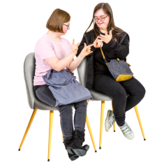 Two people sitting on a chair facing towards each other. They are using hand sign language to communicate. 