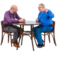 Two people sitting across each other on a round table. One person is talking and using their hands. The other person is listening. 